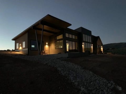 A low modern home glowing from within at dusk against a darkening ridgeline