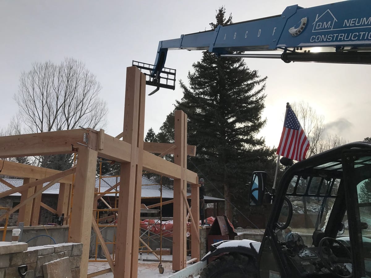 A D.M. Neuman crane setting heavy timber framing with the American flag flying from the boom