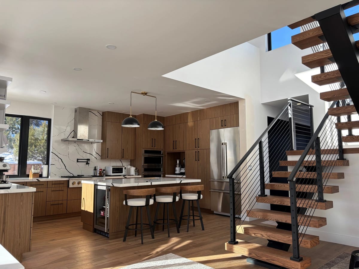 A custom kitchen beside an open-tread staircase with cable railings