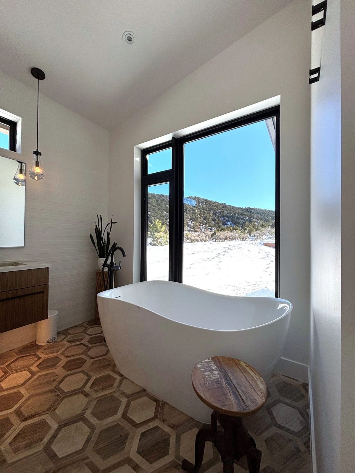 A freestanding soaking tub set in front of a window with a snowy view