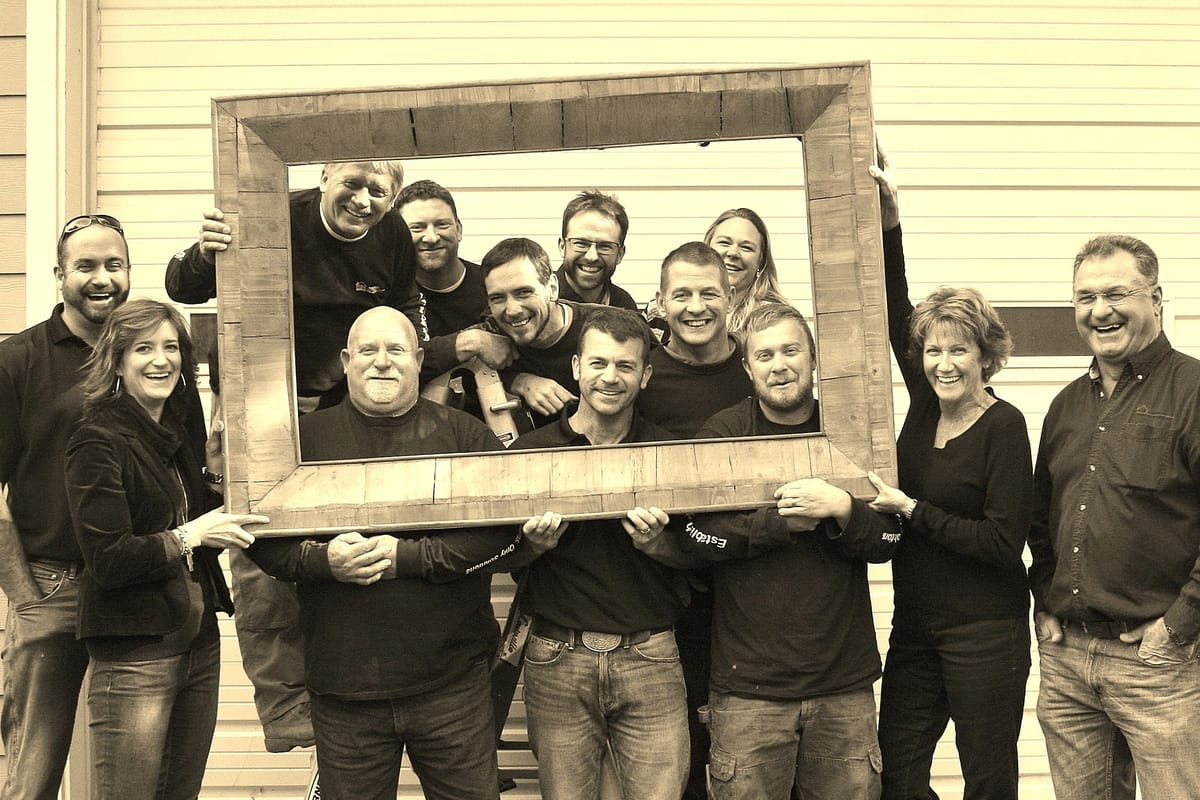 The D.M. Neuman Construction team gathered on a jobsite, holding a timber frame between them