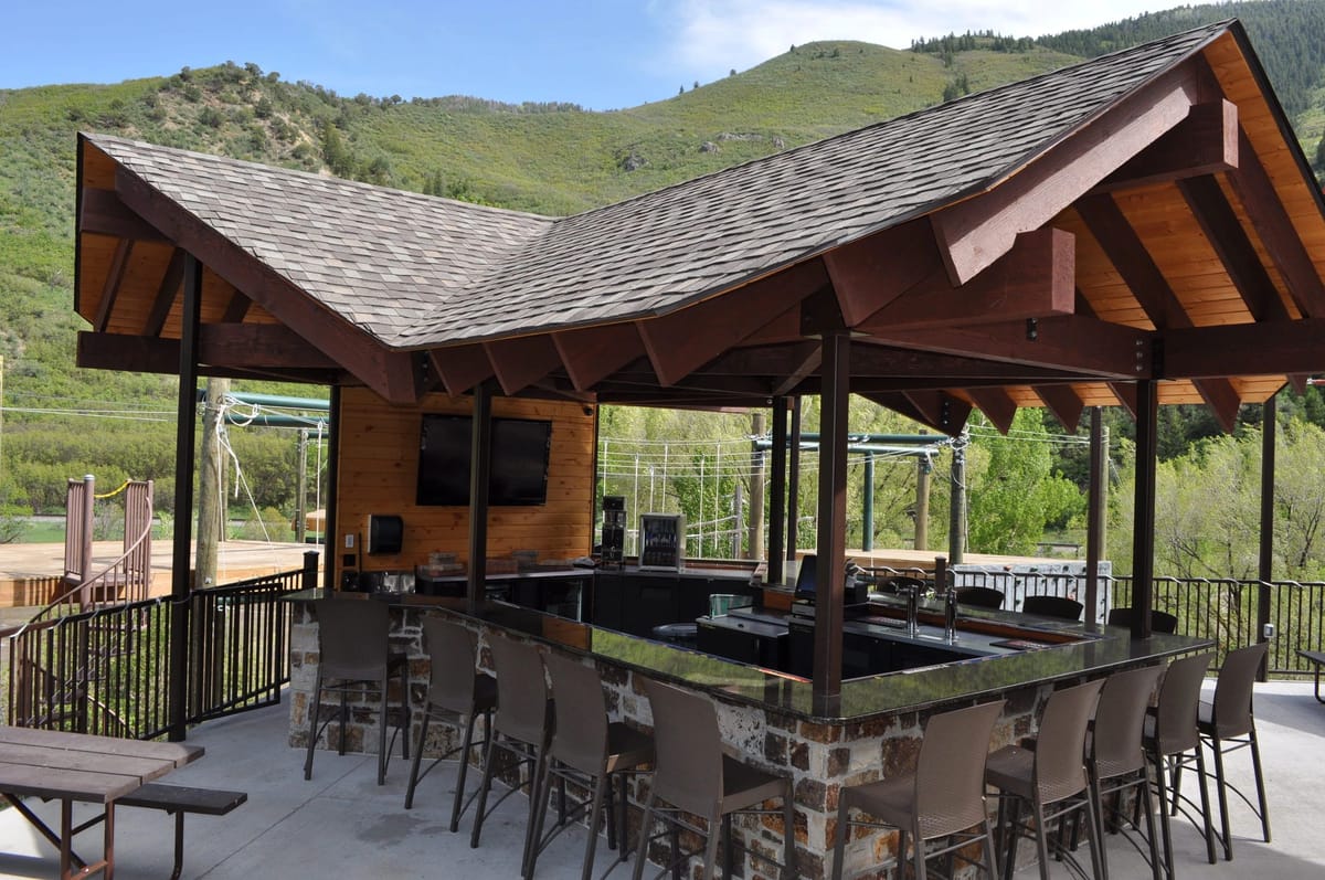 A heavy-timber outdoor pavilion with a bar and terrace overlooking green hills