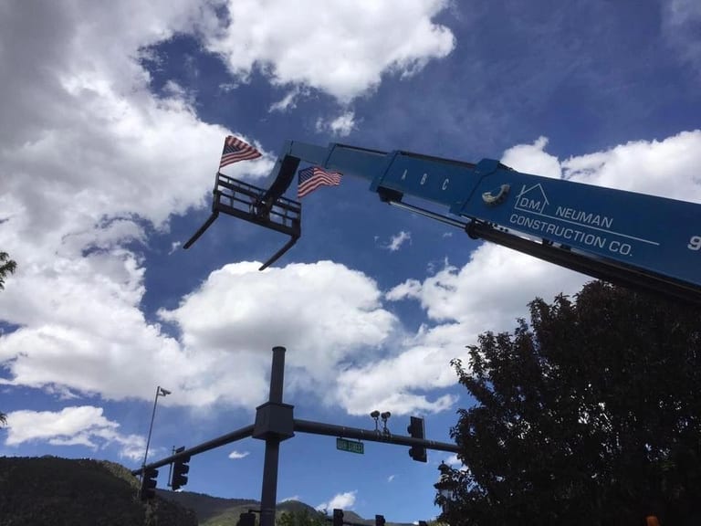 A D.M. Neuman crane boom flying the American flag against a blue sky