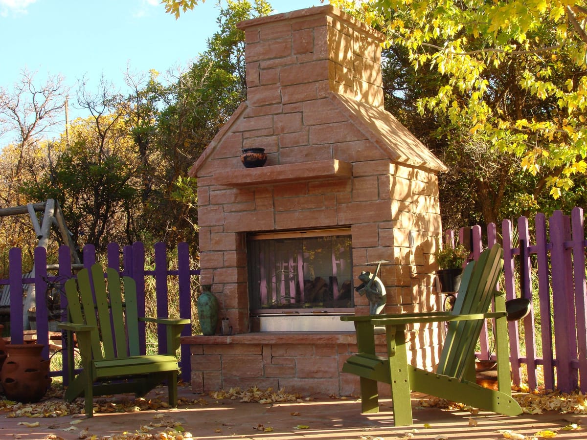 A stone outdoor fireplace with Adirondack chairs and an aspen backdrop