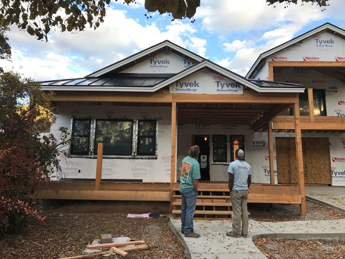 Two crew members reviewing exterior skirt detailing on a wrapped house