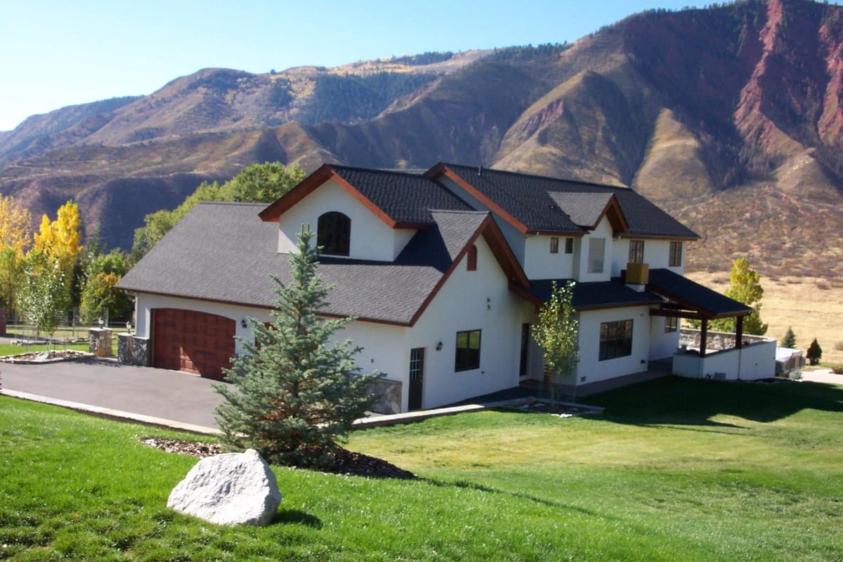 A white-and-timber custom home on a green lawn with the Glenwood hogback rising behind it