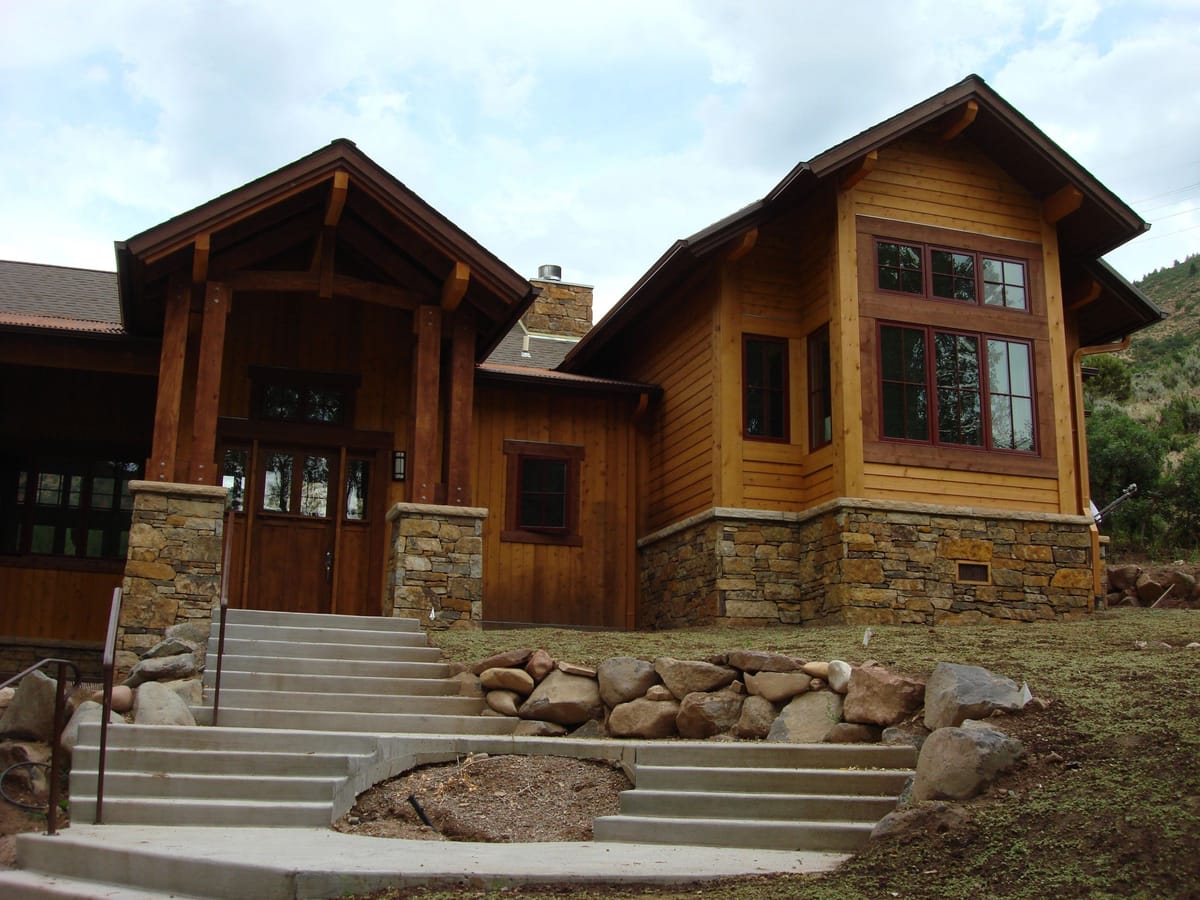 A heavy-timber mountain lodge home with stone steps and a boulder-lined entry