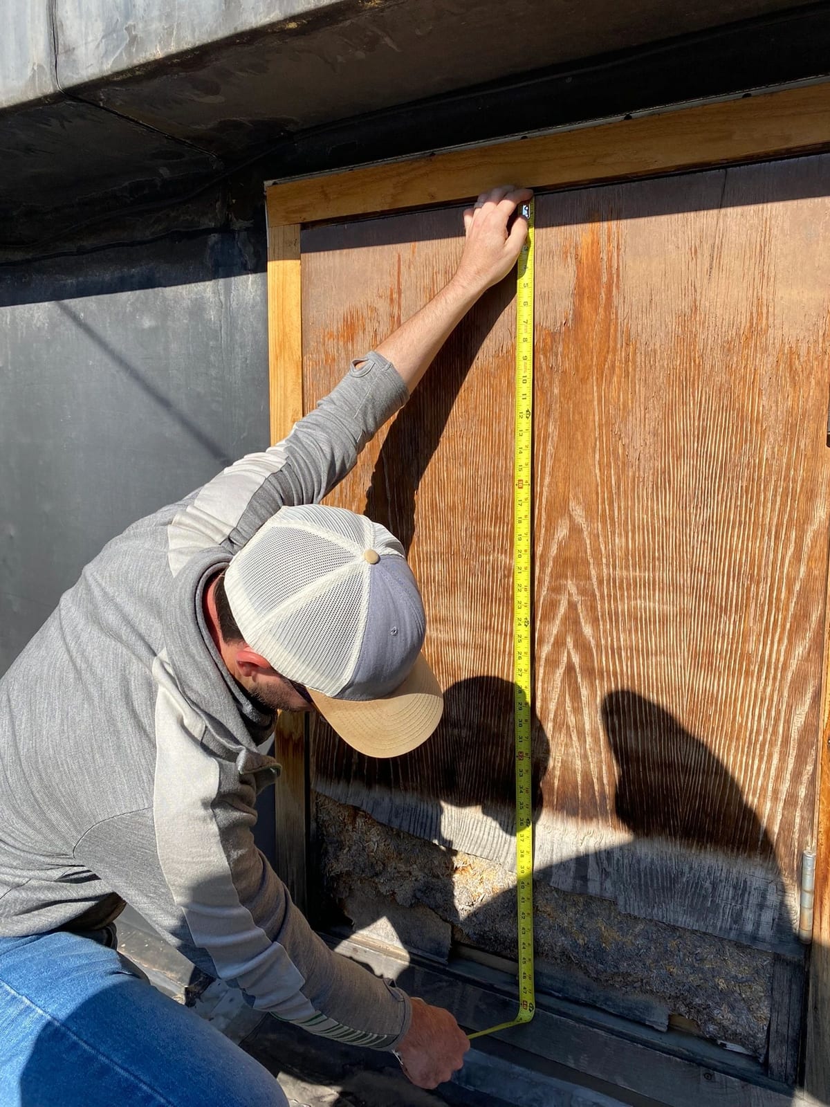 A carpenter measuring and marking a sheet of plywood on a D.M. Neuman jobsite