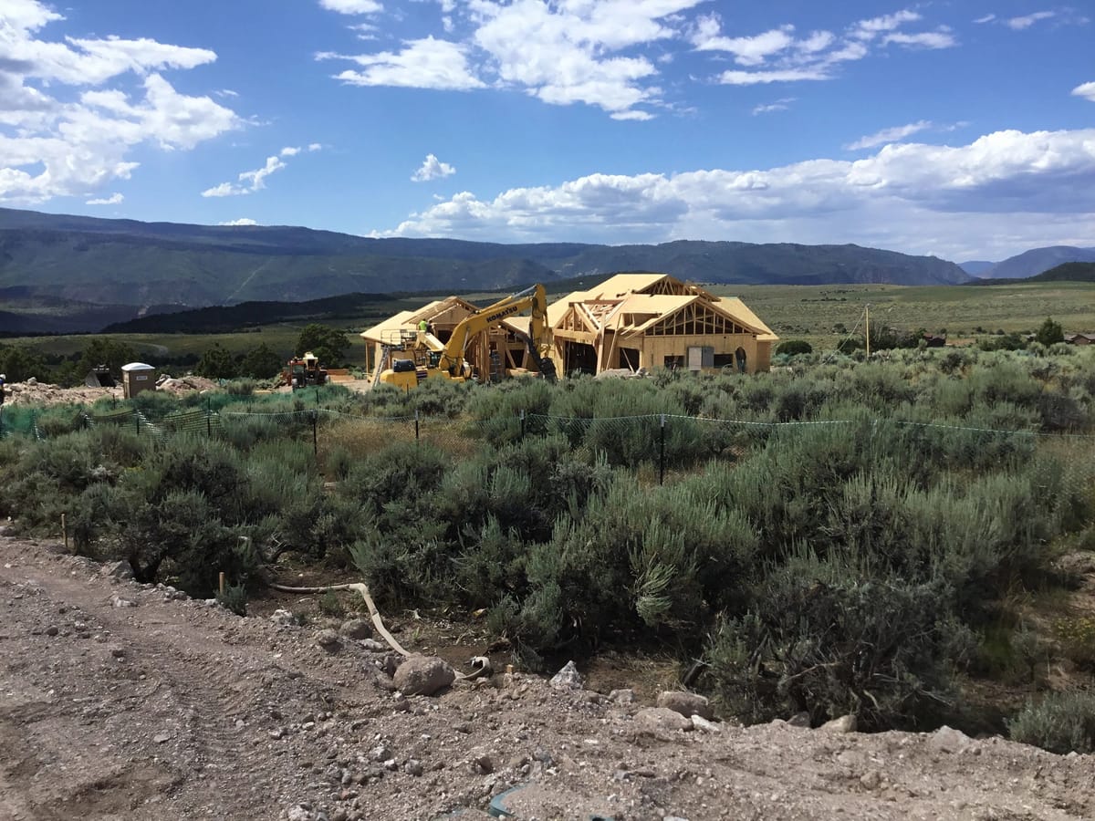 A house under frame standing in sagebrush with the Colorado range beyond