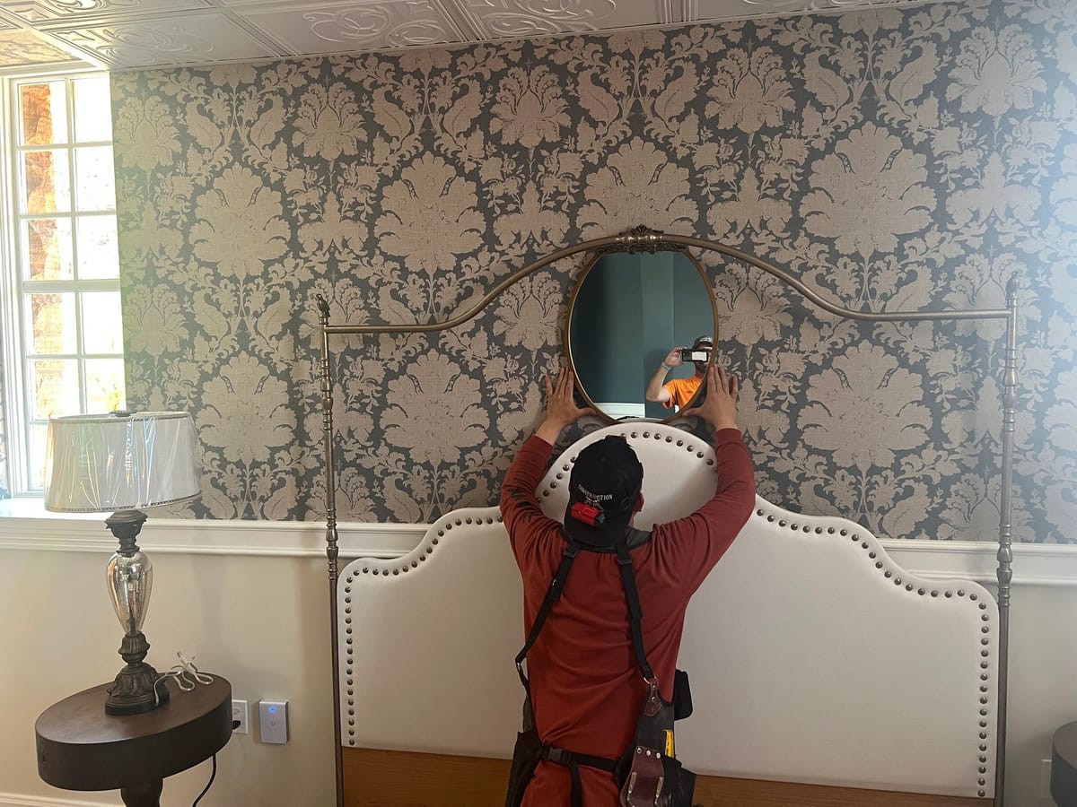 A crew member hanging a mirror during the final staging of a finished room