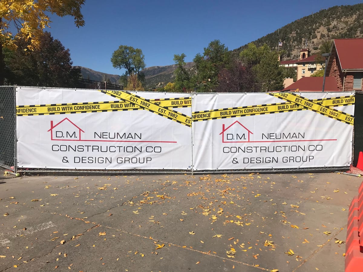 A D.M. Neuman Construction Co. banner reading Build with Confidence on a jobsite fence
