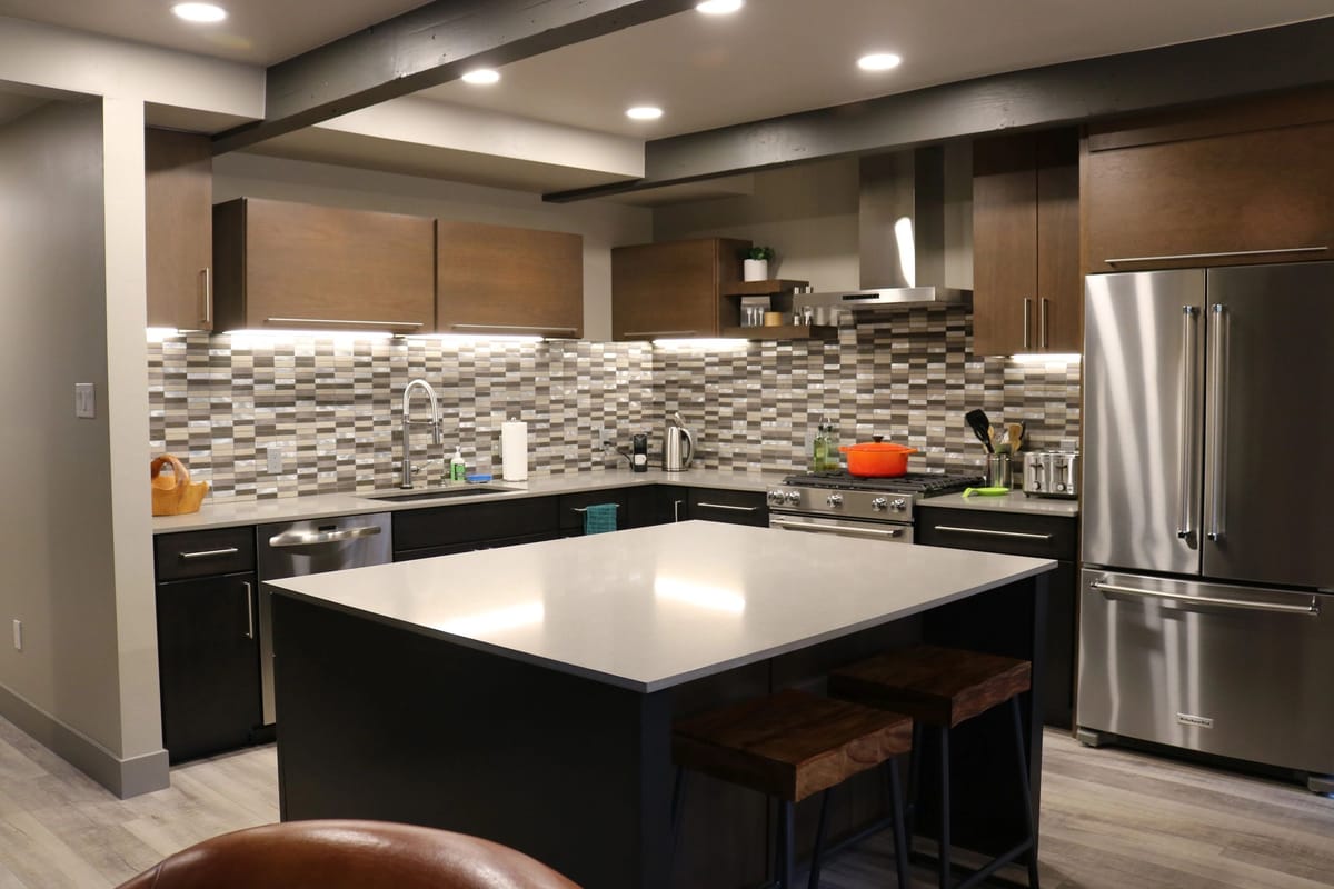 A finished custom kitchen with a large island, tile backsplash and stainless appliances