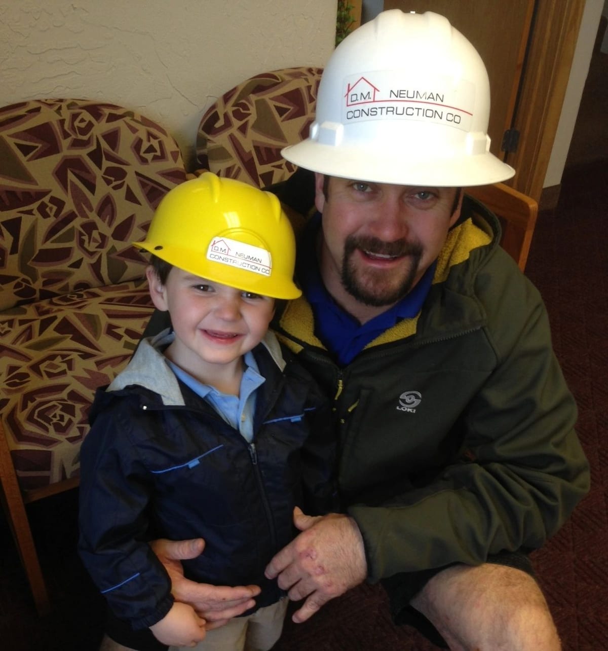 A D.M. Neuman crew member in a hard hat with a small child in a matching yellow hard hat