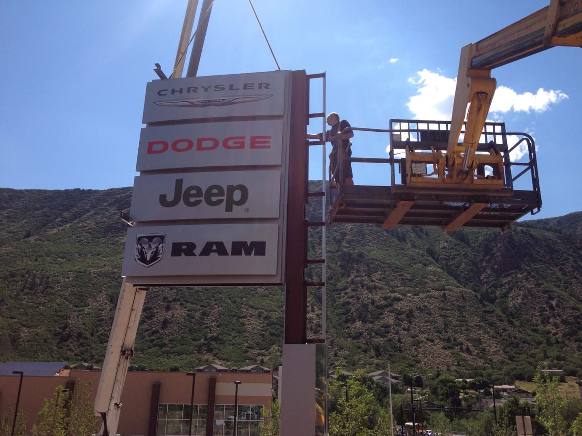 A crane lifting the Chrysler Dodge Jeep Ram sign into place above a dealership