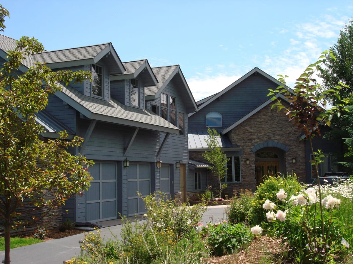A shingled residence with stone detailing and mature landscaping