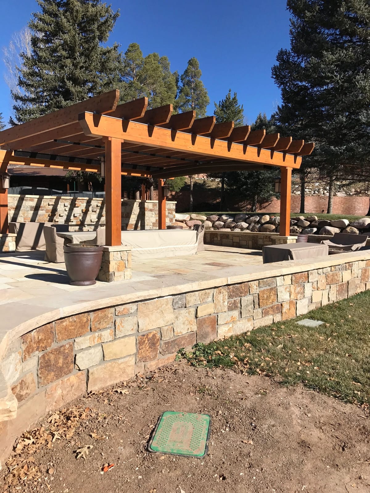 A stone patio with a timber pergola and built-in seating walls