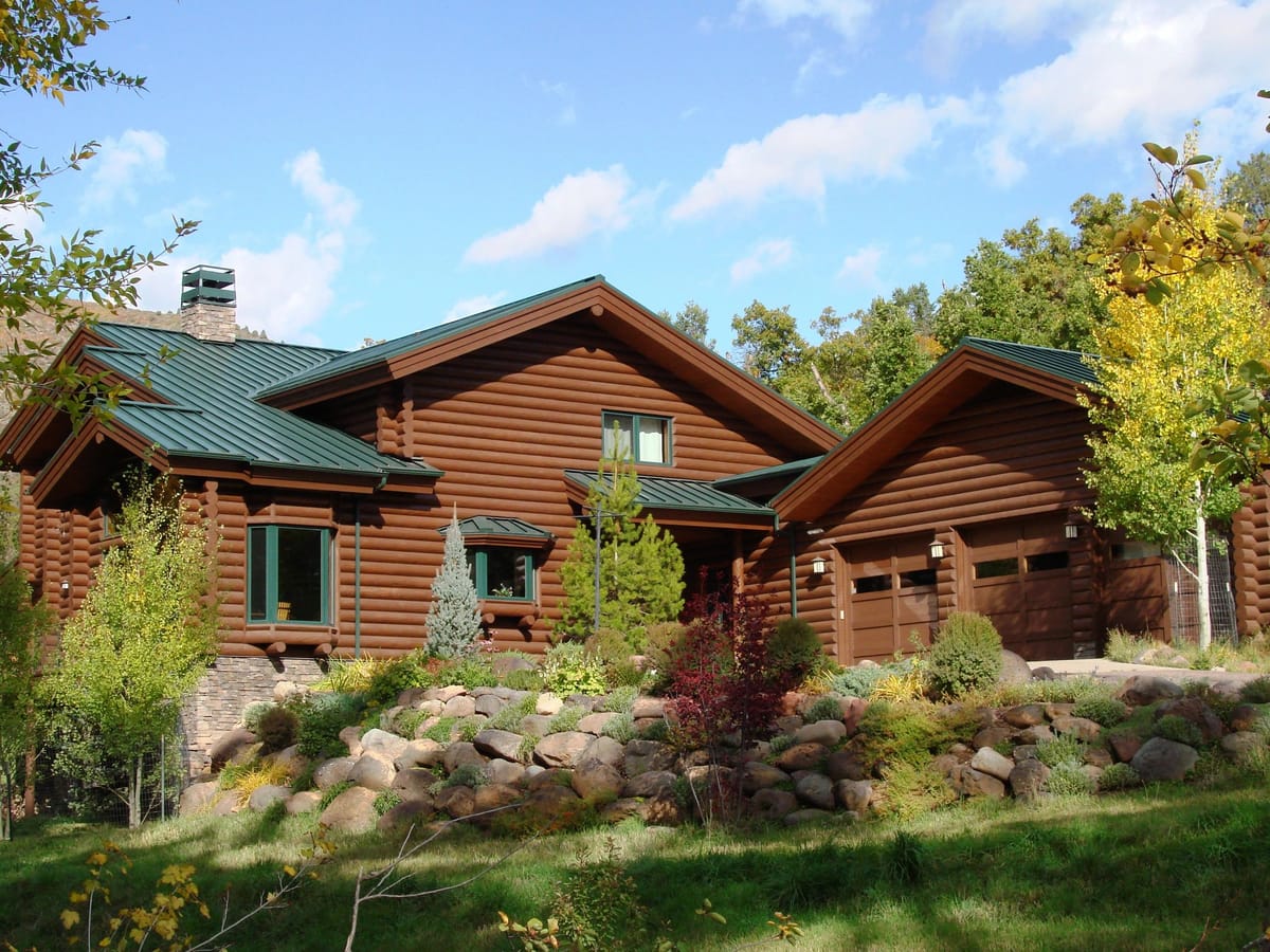 A full log home with a green metal roof and boulder landscaping