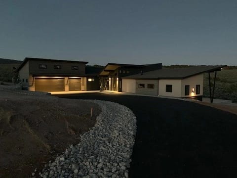 A low contemporary home glowing from within at dusk above a cut hillside